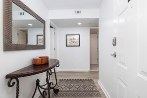 Un couloir avec une console en bois, un tableau encadré au mur et un tapis à motifs.