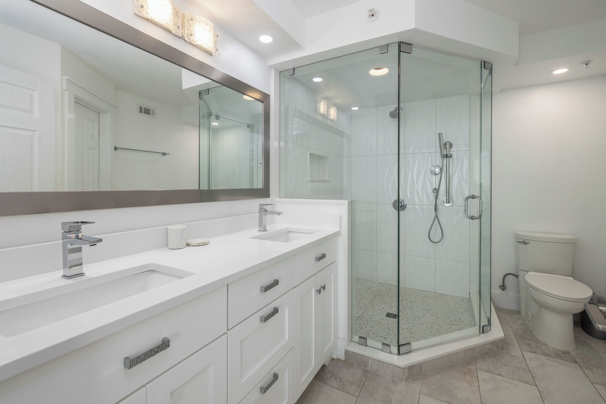 A modern bathroom with a glass-enclosed shower, white cabinetry, and a large mirror.
