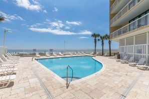 A pool area with lounge chairs and a view of the ocean.