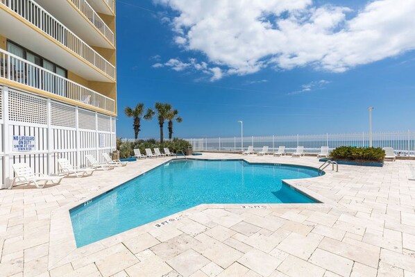 A pool area with a clear blue sky, palm trees, and a white fence.
