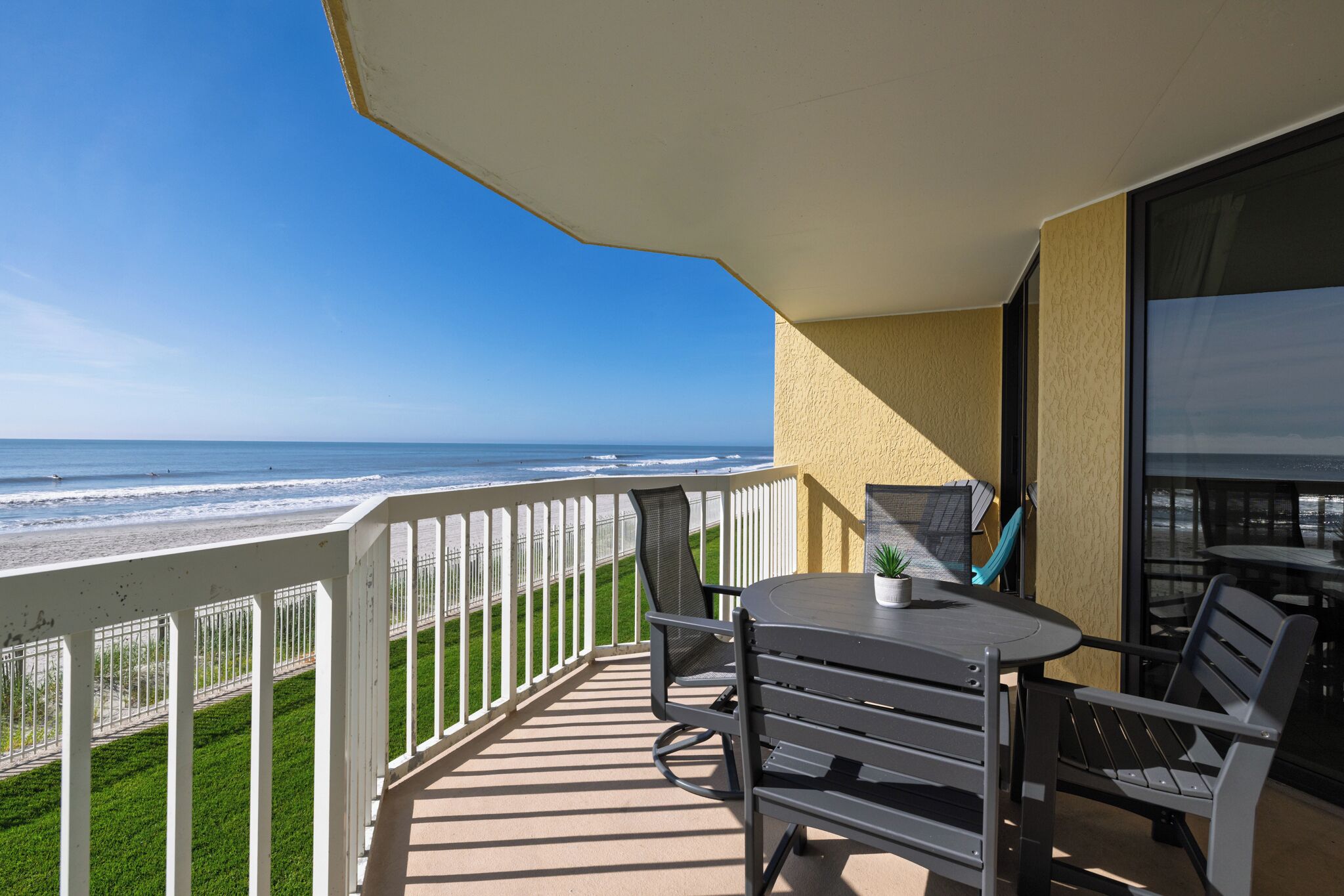 Un balcon avec vue sur la plage, une table avec des chaises et une petite plante.