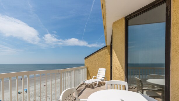 Ein Balkon mit einem weißen Tisch und Stühlen mit Blick auf einen Strand und den Ozean.