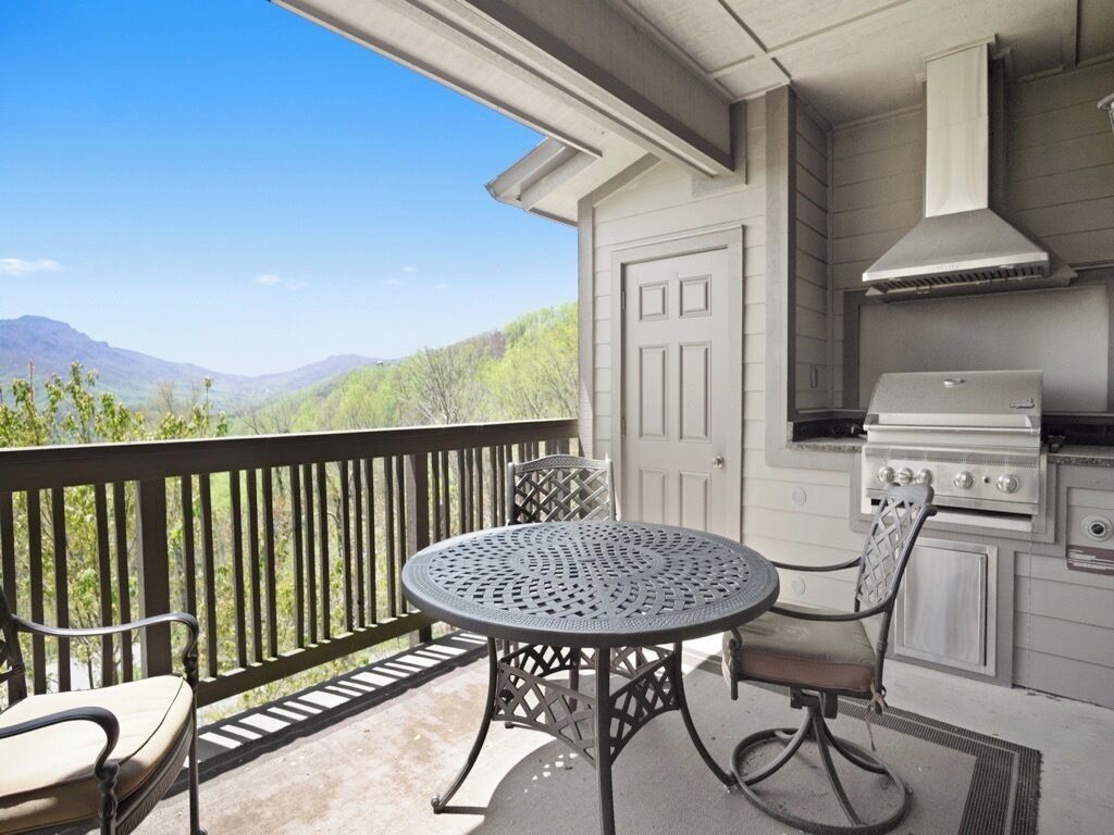 An outdoor patio with a round table and two chairs, a grill, and a door leading to a covered area.