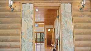 Eingang eines Holzchalets mit einem Steingewölbe, einem Holzboden und einer Bank darin.