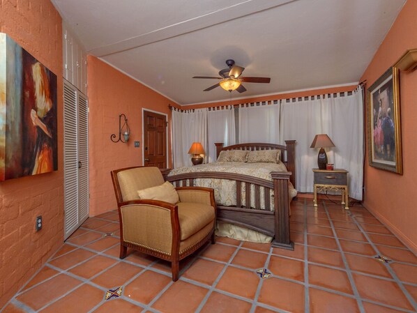 A bedroom with a bed, a chair, a nightstand, a ceiling fan, and a window with curtains.