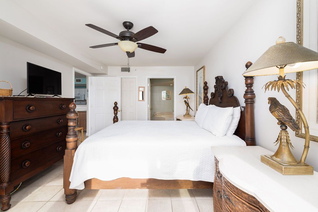 Un dormitorio con una cama grande, tocador de madera, ventilador de techo y una lámpara con escultura de pájaro.