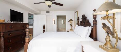 Un dormitorio con una cama grande, tocador de madera, ventilador de techo y una lámpara con escultura de pájaro.