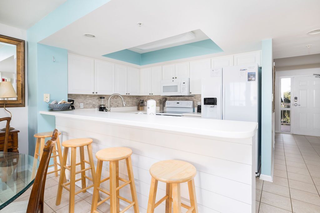 A modern kitchen with white cabinets, a central island with stools, a microwave, and a refrigerator.