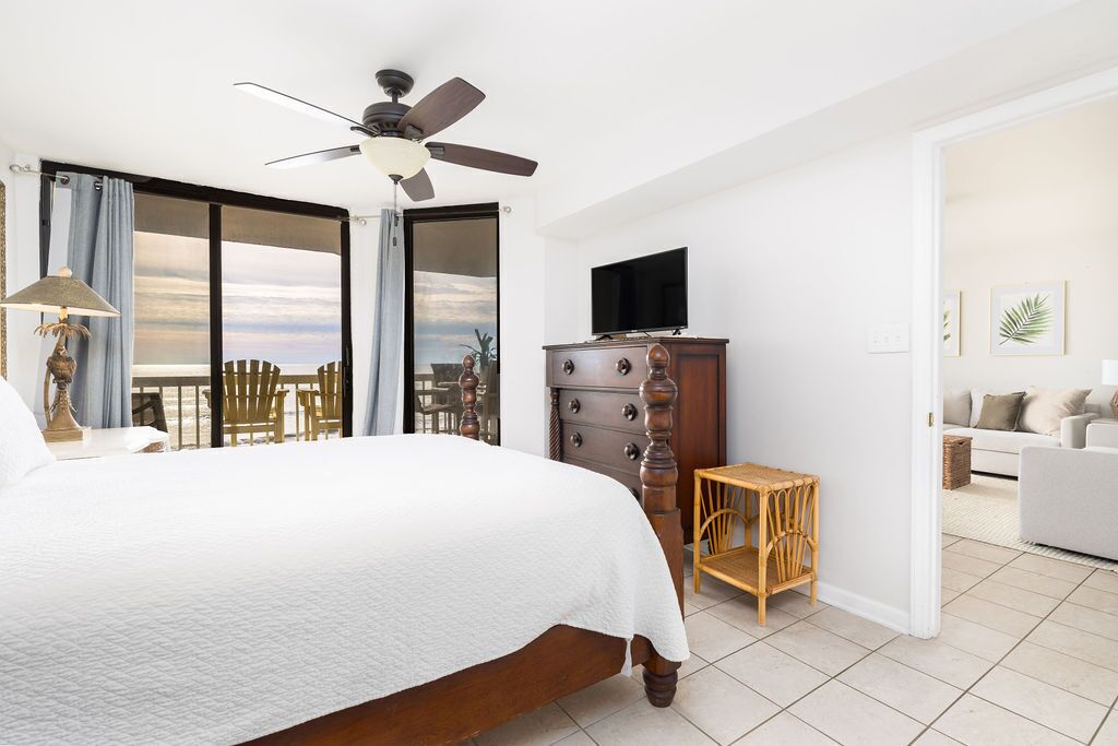 Ein Hotelzimmer mit einem großen Bett, einem Deckenventilator, einem Fernseher, einer Holzkommode und einem Balkon mit Aussicht.