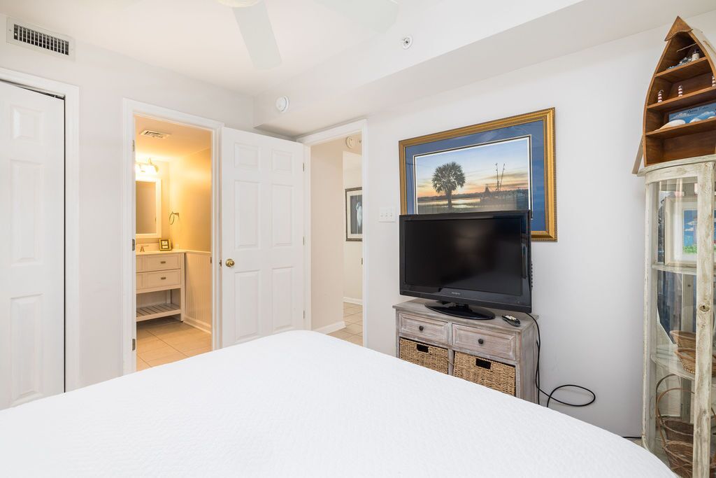 A bedroom with a bed, a television on a wooden stand, a framed picture on the wall, and a cabinet with baskets.