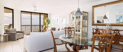A spacious living room with a glass dining table, white sofas, and wooden chairs.