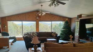 A cozy living room with a large window, a ceiling fan, a television, and a Christmas tree.