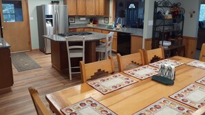 A modern kitchen with wooden cabinets, a stainless steel refrigerator, and a dining area with a wooden table and chairs.