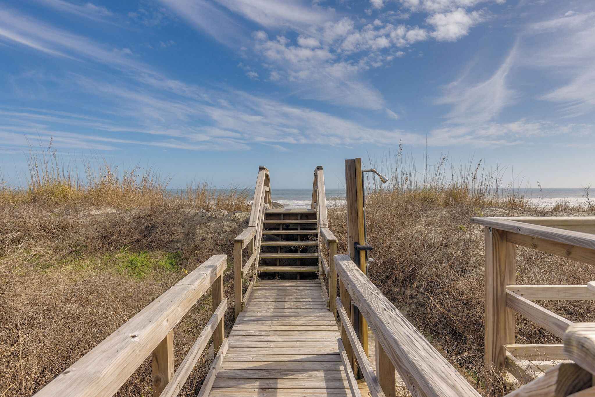 Une promenade en bois menant à une plage, avec un ciel dégagé.