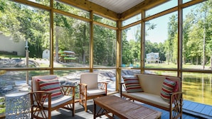 A covered outdoor seating area with wooden furniture and a view of a lake and trees.