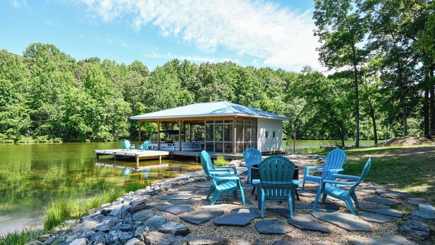 A lakeside cabin with a covered patio, stone steps, and blue Adirondack chairs.