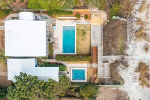 Vista aerea di una proprietà con un ampio edificio bianco, una piscina e una zona con pavimento in legno.