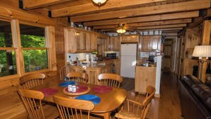 A wooden cabin interior with a dining area, kitchen, and a living room with a sofa. - Riverfront New River Cabin - Relax and Renew - Family Cabin Near Boone (Todd)