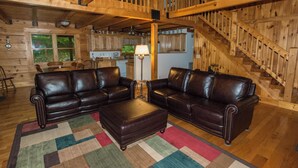 A log cabin interior with two leather sofas, a wooden staircase, and a kitchen area. - Riverfront New River Cabin - Relax and Renew - Family Cabin Near Boone (Todd)