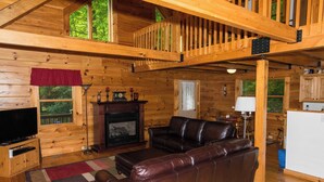 A cozy log cabin interior with a fireplace, leather sofa, wooden floors, and a balcony. - Riverfront New River Cabin - Relax and Renew - Family Cabin Near Boone (Todd)