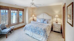 Une chambre avec un grand lit, deux tables de chevet avec des lampes, une chaise et un ventilateur de plafond.