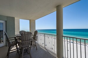 Een balkon met een tafel en stoelen, uitkijkend op een strand.