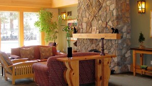 A cozy lobby with a stone fireplace, wooden furniture, and a large window offering a view of the outdoors.