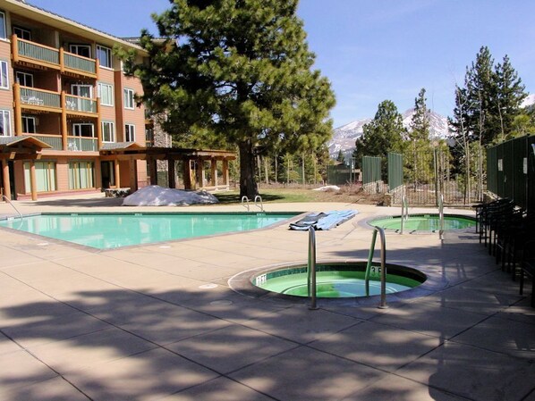 Zona de piscina de hotel con dos albercas, un área de descanso techada y vista a la montaña.