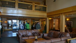 A spacious lobby with leather sofas, a coffee table, and a wooden balcony.