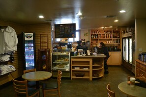 Una cafetería con mostrador, zona de estar y vitrina refrigerada.