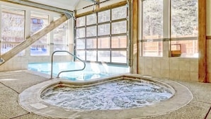 A hot tub with a view of a pool and a wooden staircase.