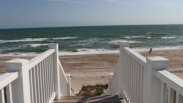 A wooden staircase leading to a beach with ocean views.