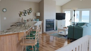 A kitchen with a marble countertop, wooden chairs, a TV, and a ceiling fan.