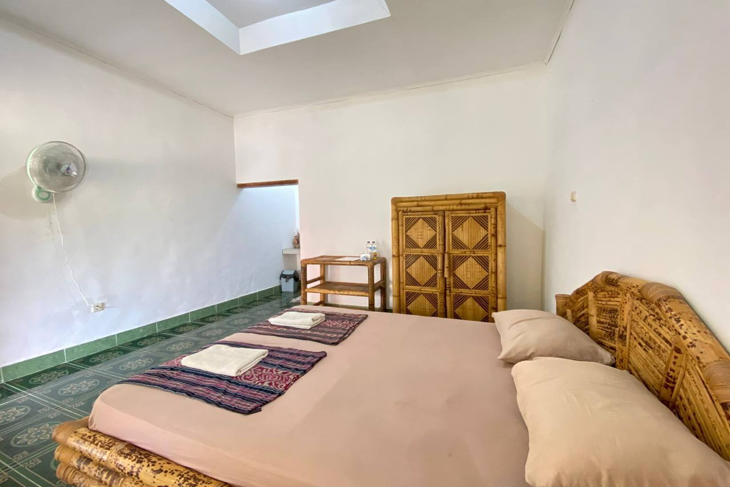 A room with a bed, a wooden headboard, a small table, and a wall-mounted fan.