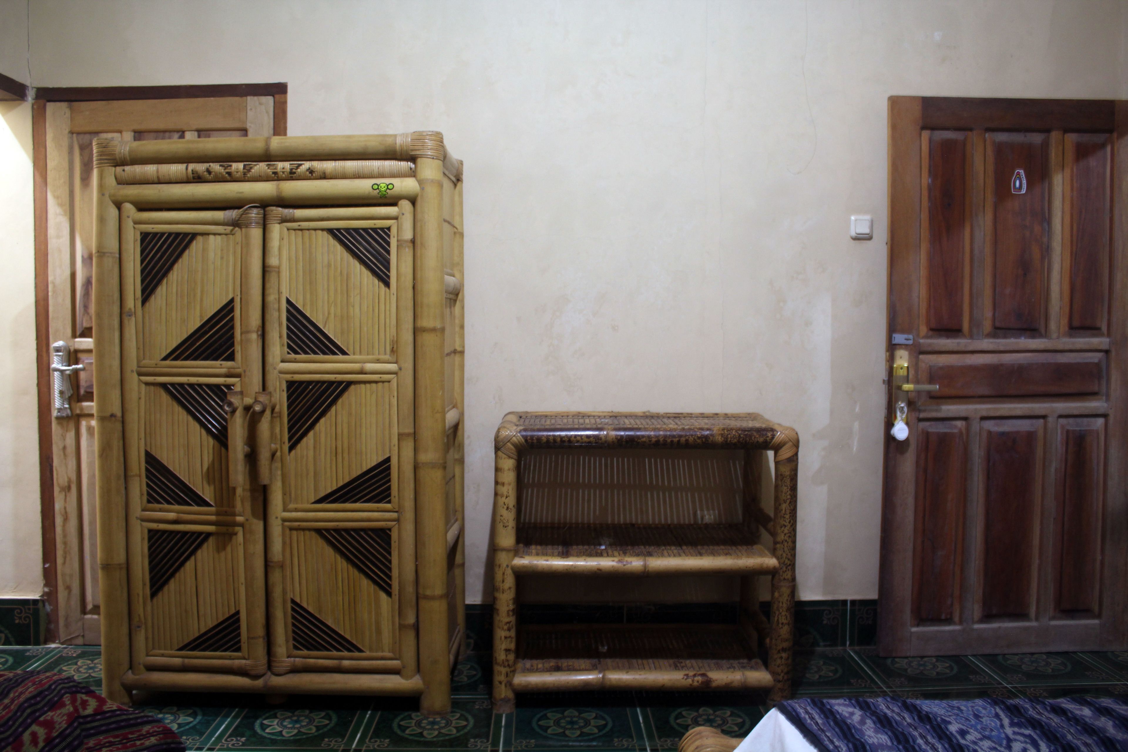 Una habitación con un amplio armario de bambú, una pequeña silla de mimbre y una puerta de madera.