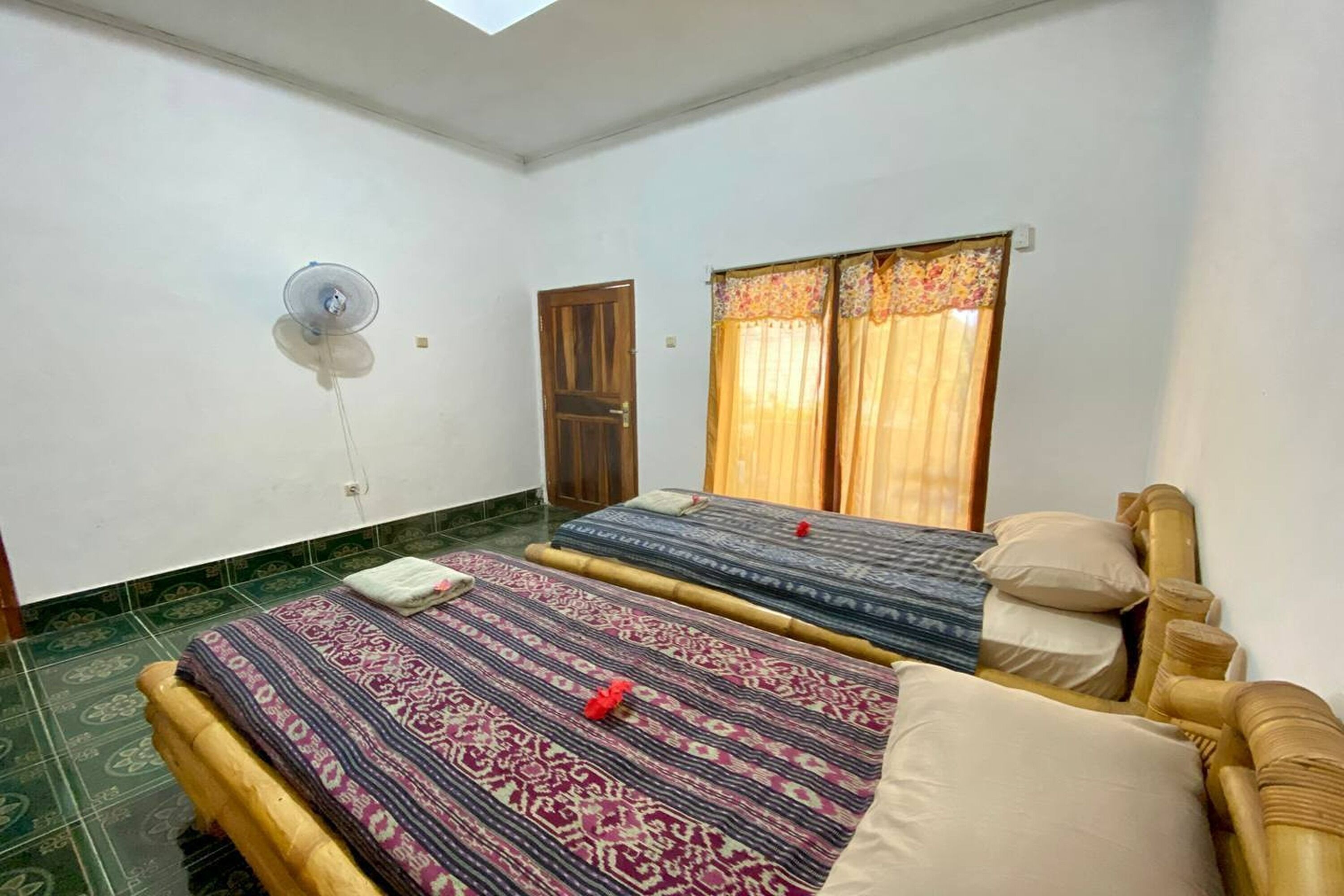 Una habitación con dos camas, un ventilador, una puerta y una ventana con cortinas.