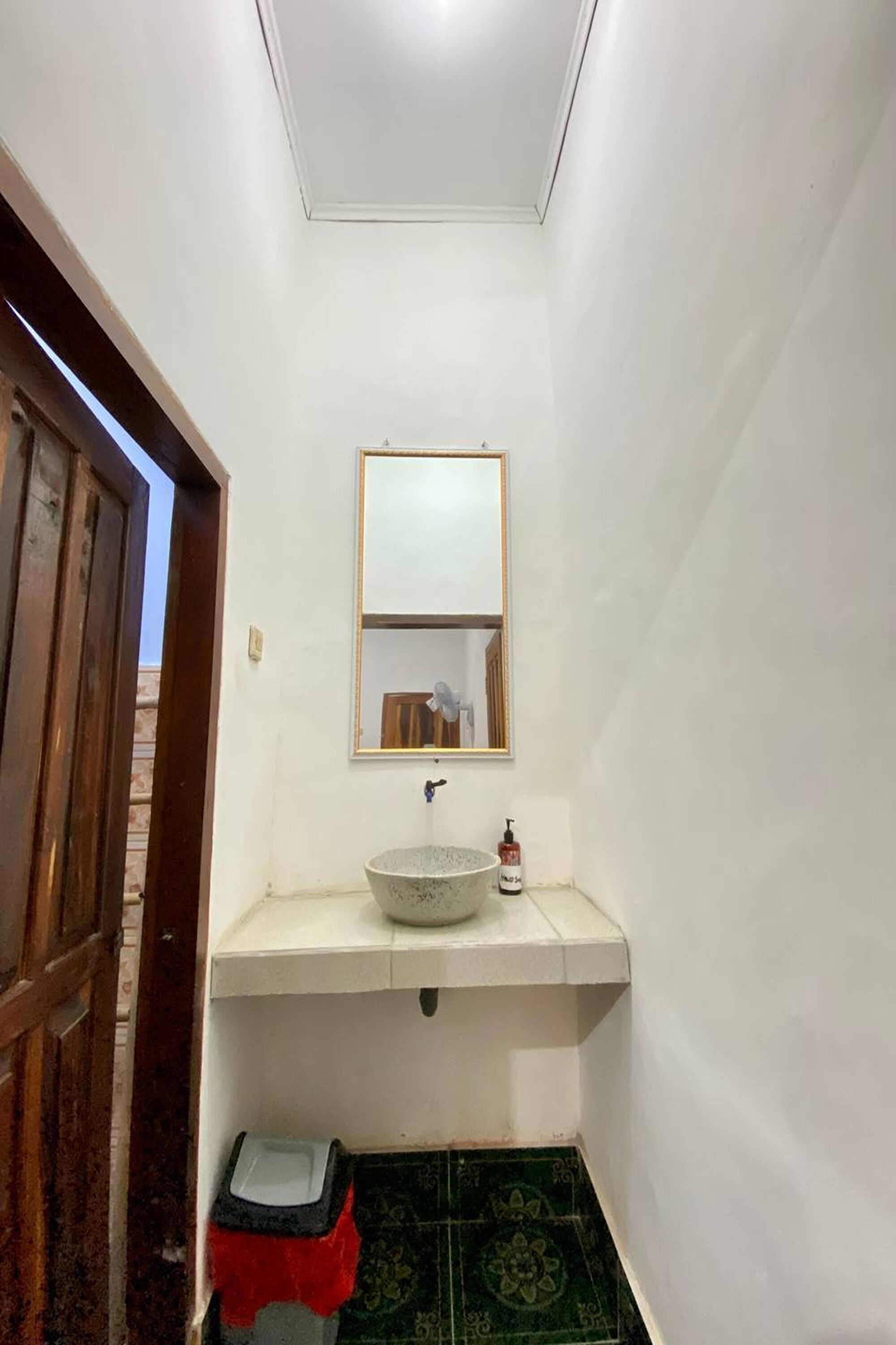 A small bathroom with a white sink, a mirror above it, and a trash bin below.