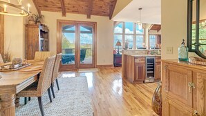 Una cocina amplia con suelo de madera, un comedor con sillas de mimbre y un gran ventanal con vistas al exterior.