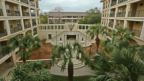 A multi-story hotel with balconies, a central courtyard with palm trees, and a staircase leading to the upper floors. - 301 North Shore End Unit, No carpet, CLEAN, Wrap-around Balcony, August Avail. (Hilton Head Island)
