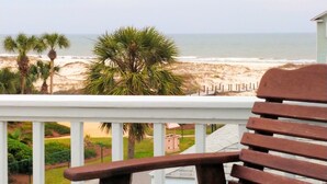 A wooden chair with a teal cushion on a balcony overlooking a beach with palm trees and a fence. - AT THE BEACH!  Beautiful 3 Bed and 3 Bath (Gulf Shores)