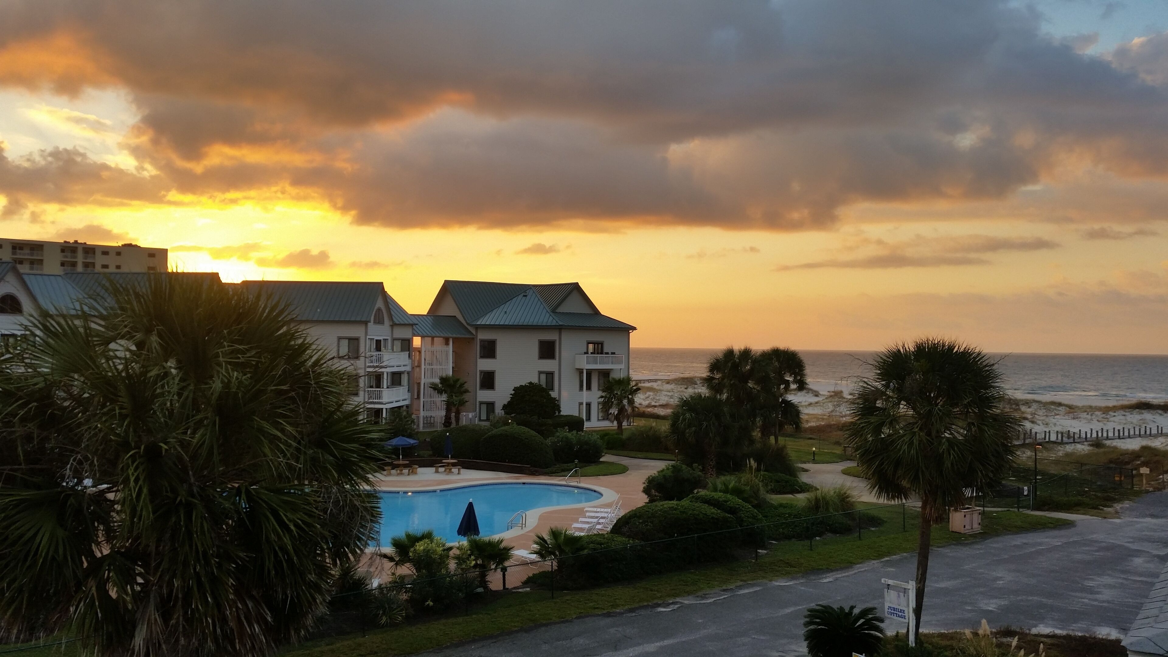 Ein Resort mit Schwimmbad, Blick auf den Strand und einem zweistöckigen Gebäude mit Balkon.