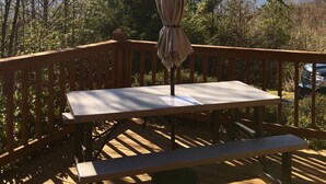 A wooden deck with a table and bench, an umbrella, and a view of mountains and trees.