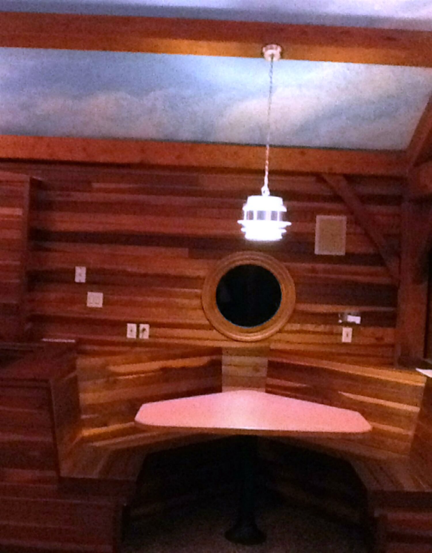 Interno di una baita in legno con un lucernario circolare, un lampadario e una panca di legno.