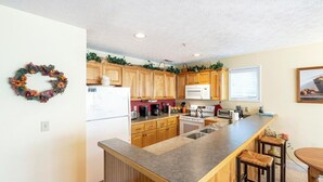 Una cocina con armarios de madera, una isla integrada, un refrigerador, un microondas y un lavamanos.