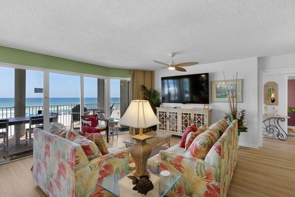 A living room with a sofa, a TV, and a balcony with a view of the ocean.