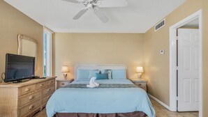 Une chambre à coucher avec un lit, un téléviseur posé sur une commode et un ventilateur de plafond.
