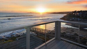 A coastal sunset view from a balcony with a railing, overlooking the sea and a rocky shoreline. - Villa Vista Upper (Santa Cruz)