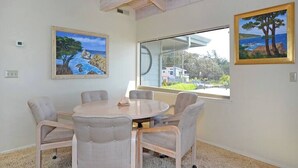A room with a round table and six chairs, large windows with a view of the sea, and two framed paintings on the walls. - Villa Vista Upper (Santa Cruz)