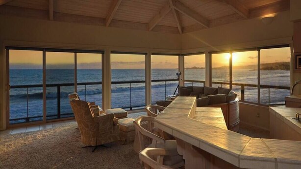 A spacious room with a curved bar, large windows, and a view of the ocean at sunset. - Villa Vista Upper (Santa Cruz)