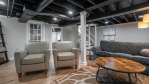 Et moderne interiør med højt til loftet, synlige bjælker og en trappe til en etage ovenover. To lænestole, en stribet sofa og et rundt sofabord.
